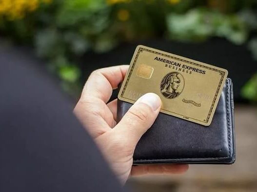 The American Express® Gold Card being held up in front of a bright blue wall