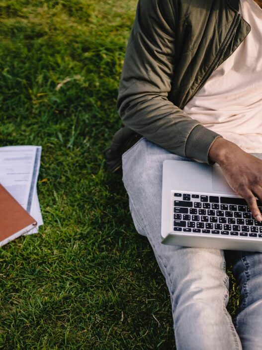 student with laptop and papers on green lawn