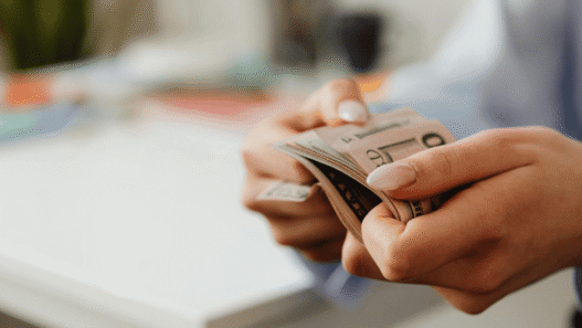 Woman with manicured nails holding a wad of cash of cash bill against blurred background. Photo by Photo By: Kaboompics.com: