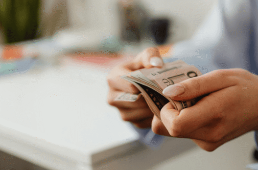 Woman with manicured nails holding a wad of cash of cash bill against blurred background. Photo by Photo By: Kaboompics.com: