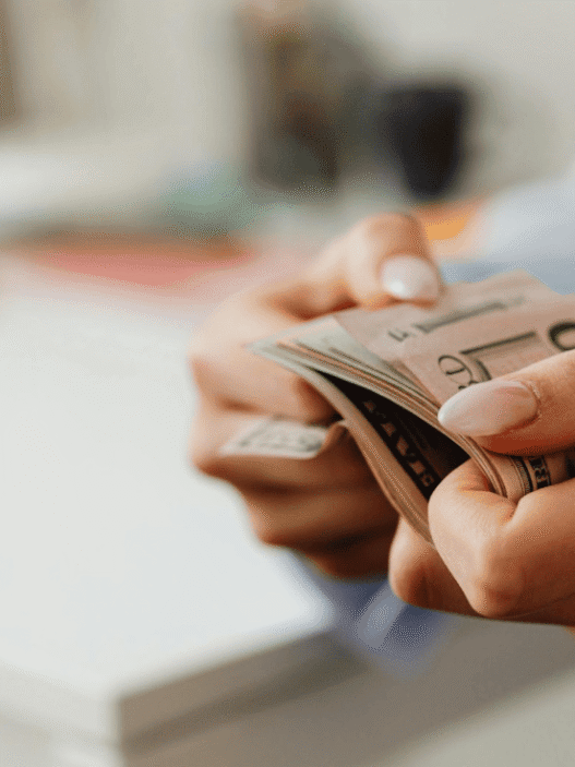 Woman with manicured nails holding a wad of cash of cash bill against blurred background. Photo by Photo By: Kaboompics.com: