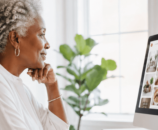 Mature Black woman working on Pinterest at her computer in a light, modern home office, researching ideas and content strategy in a calm, minimalist workspace. She is searching for pinterest hacks